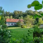 Ein Haus mit rotem Dach, umgeben von üppig grünen Bäumen und einem gepflegten Rasen.